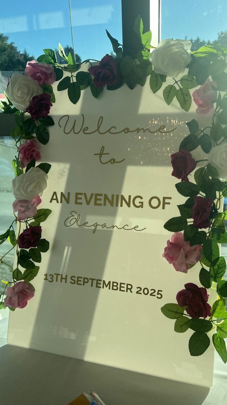 A welcome sign framed with pink and white roses. It reads: Welcome to An Evening of Elegance, 13th September 2025.
